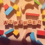 Drewniane klocki z literami układające się w słowo Asperger na jasnym dywanie. Temat: asperger a autyzm.