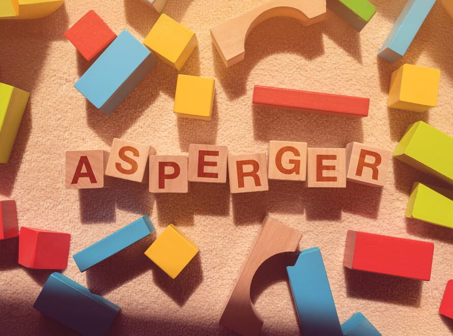 Drewniane klocki z literami układające się w słowo Asperger na jasnym dywanie. Temat: asperger a autyzm.