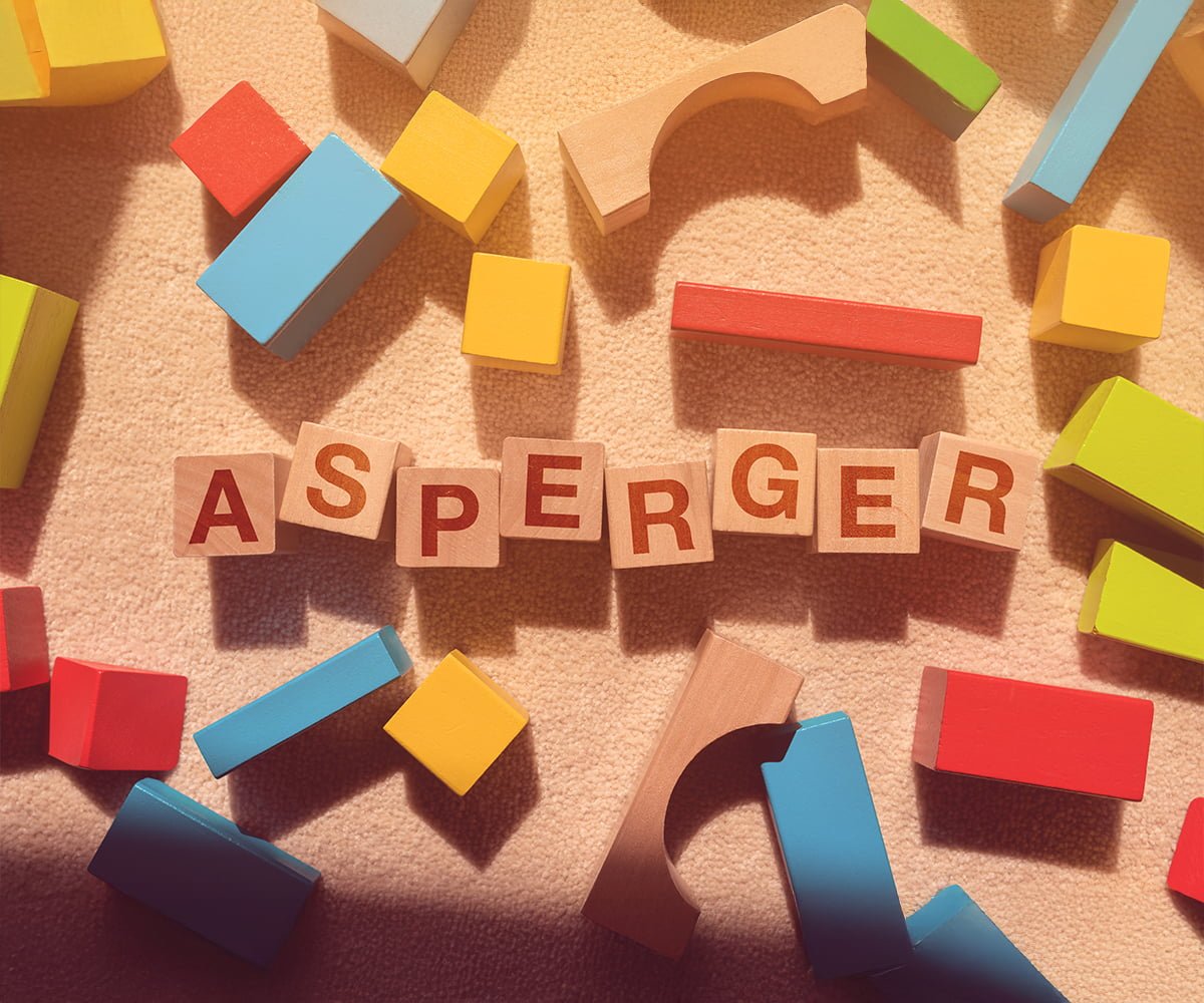 Drewniane klocki z literami układające się w słowo Asperger na jasnym dywanie. Temat: asperger a autyzm.